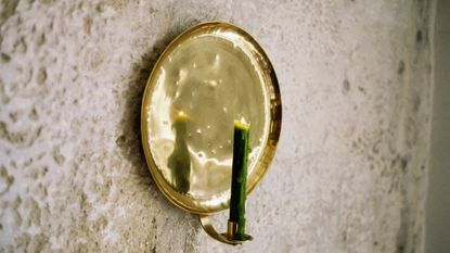 Pooky's Bellamy Candle Sconce styled with a lit moss green taper candle against a textured exterior wall