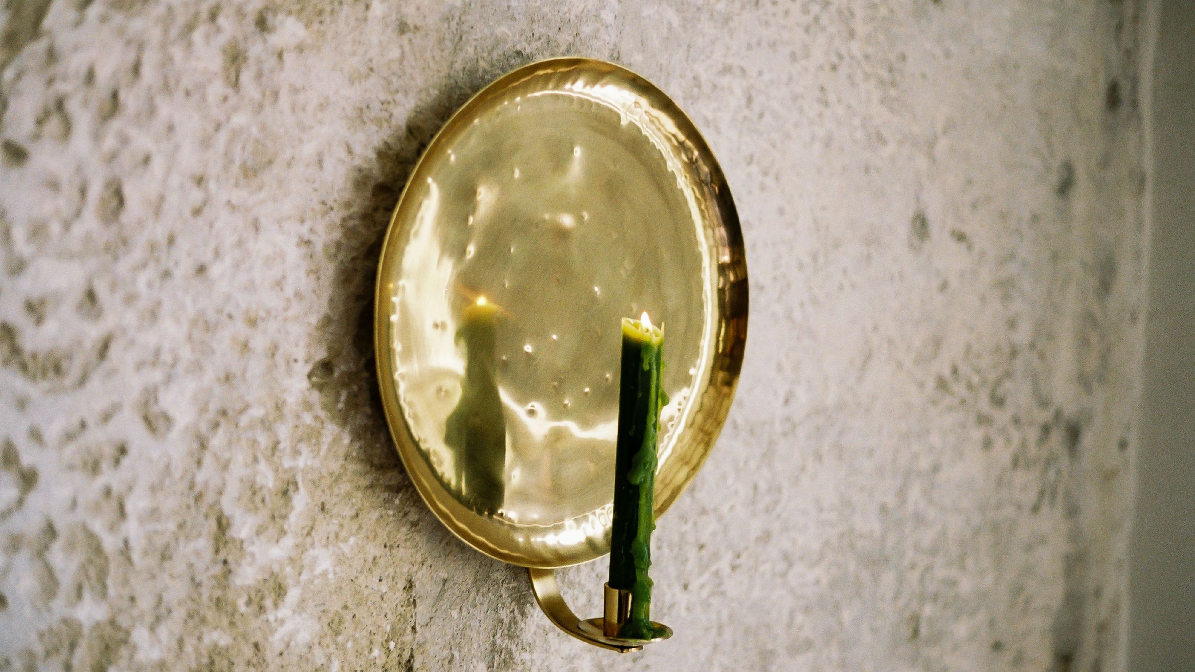 Pooky's Bellamy Candle Sconce styled with a lit moss green taper candle against a textured exterior wall
