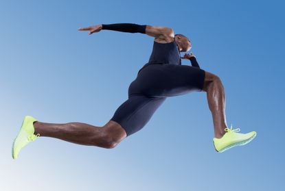 A male sprinter in motion wearing a black one piece and bright green trainers.