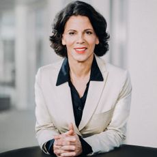 Alexandra Palt in a white suit, looking at the camera, smiling 