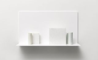 Five porcelain vessels and three alabaster blocks in light gray, light yellow, and light blue are set on a white shelf.