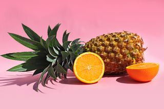 Summer theme set-up with pineapple and sunglasses along with wine glasses and orange slices placed against pink background.