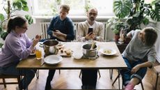A family of four sit at the kitchen table looking at their phones rather than talking to one another.