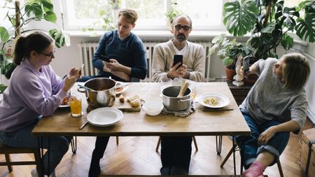 A family of four sit at the kitchen table looking at their phones rather than talking to one another.