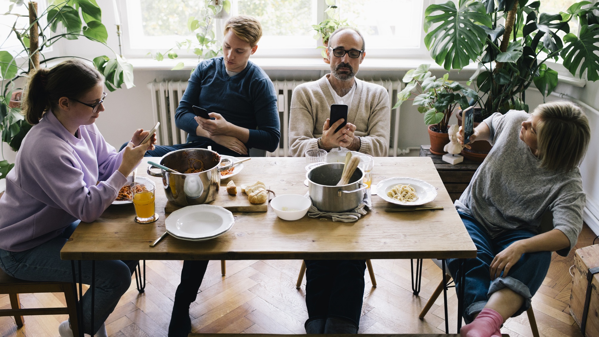 A family of four sit at the kitchen table looking at their phones rather than talking to one another.