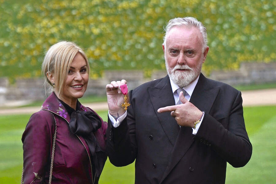 Queen drummer Roger Taylor (R), flanked by his wife Sarina (L), poses after being appointed an OBE, during an investiture ceremony at Windsor Castle, on March 30, 2022
