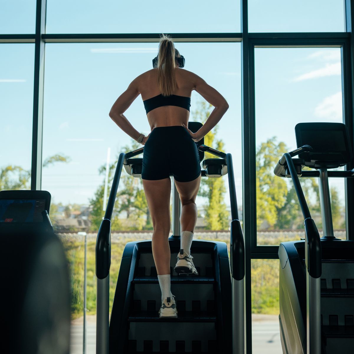 A woman stretching at the gym: arms above head, after a Stairmaster workout
