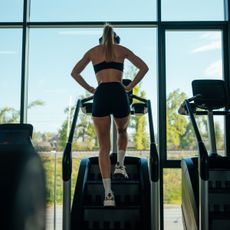 A woman stretching at the gym: arms above head, after a Stairmaster workout