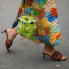 : A guest wears a multicolored print pattern quilted oversized belted long jacket, a green shiny leather with green / white / black pearls straps handbag, brown puffy satin / open toe-cap heels mules , outside Helmstedt, during the Copenhagen Fashion Week Spring/Summer 2024 on August 10, 2023 in Copenhagen, Denmark. 