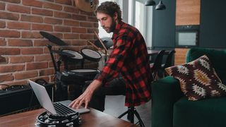Man views a drum lesson on his laptop while sat at his electronic drum kit