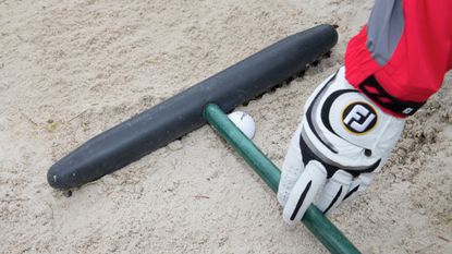 Ball resting against rake in bunker