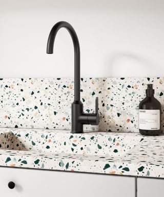 A contemporary kitchen sink with a terrazzo countertop and integrated sink featuring multicoloured stone chips in a white base. The setup includes a matte black Harbour Icon single-lever mixer tap with a sleek, curved design.