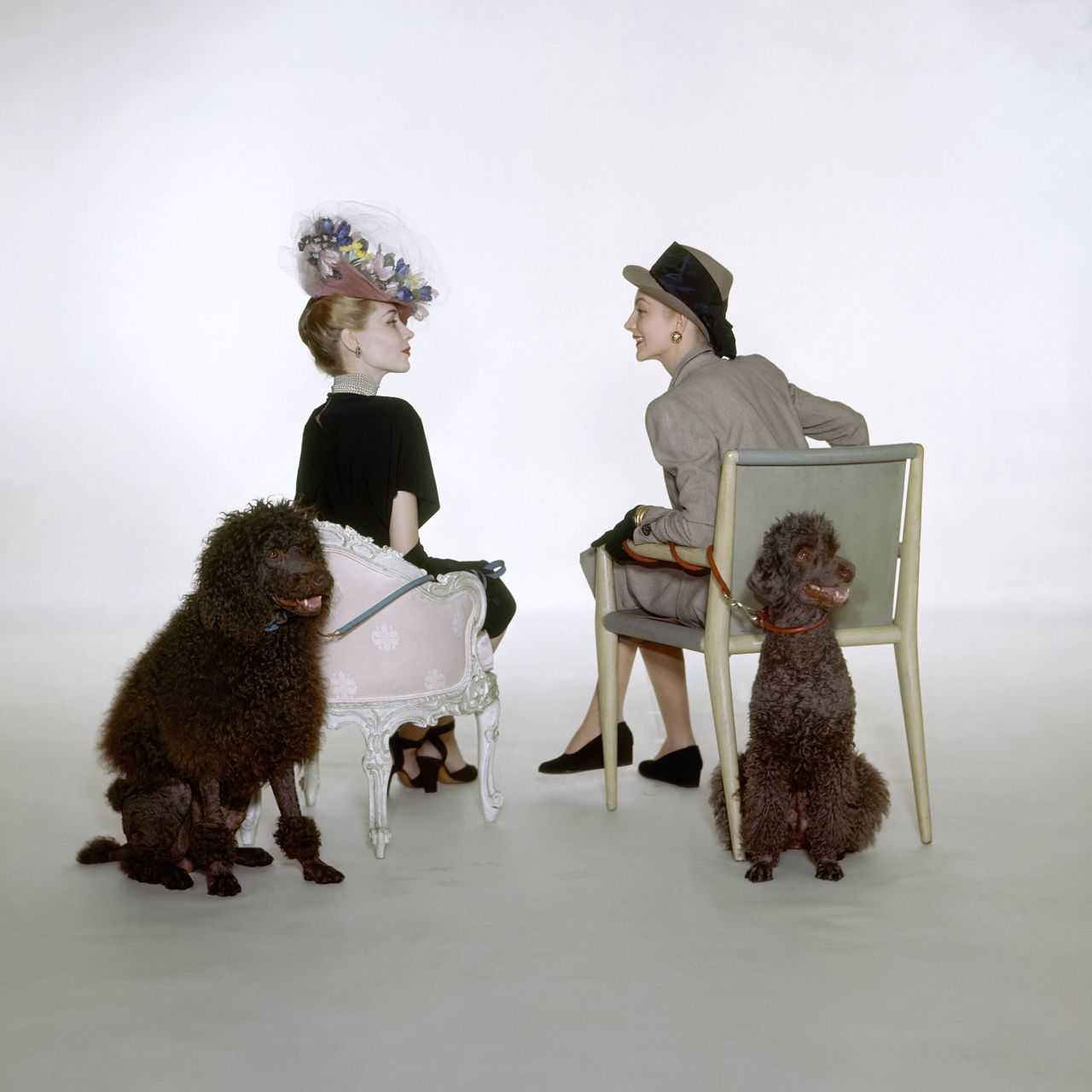 Two models, both with poodles, wearing contrasting ensembles of traditional and forward, both from Sophie of Saks Fifth Avenue.