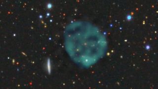 The ghostly ORC1 (blue/green fuzz), on a backdrop of the galaxies at optical wavelengths. There’s an orange galaxy at the centre of the ORC, but we don’t know whether it’s part of the ORC, or just a chance coincidence. 