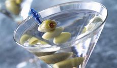 A martini glass with a clear drink and olive in it.