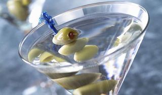 A martini glass with a clear drink and olive in it.