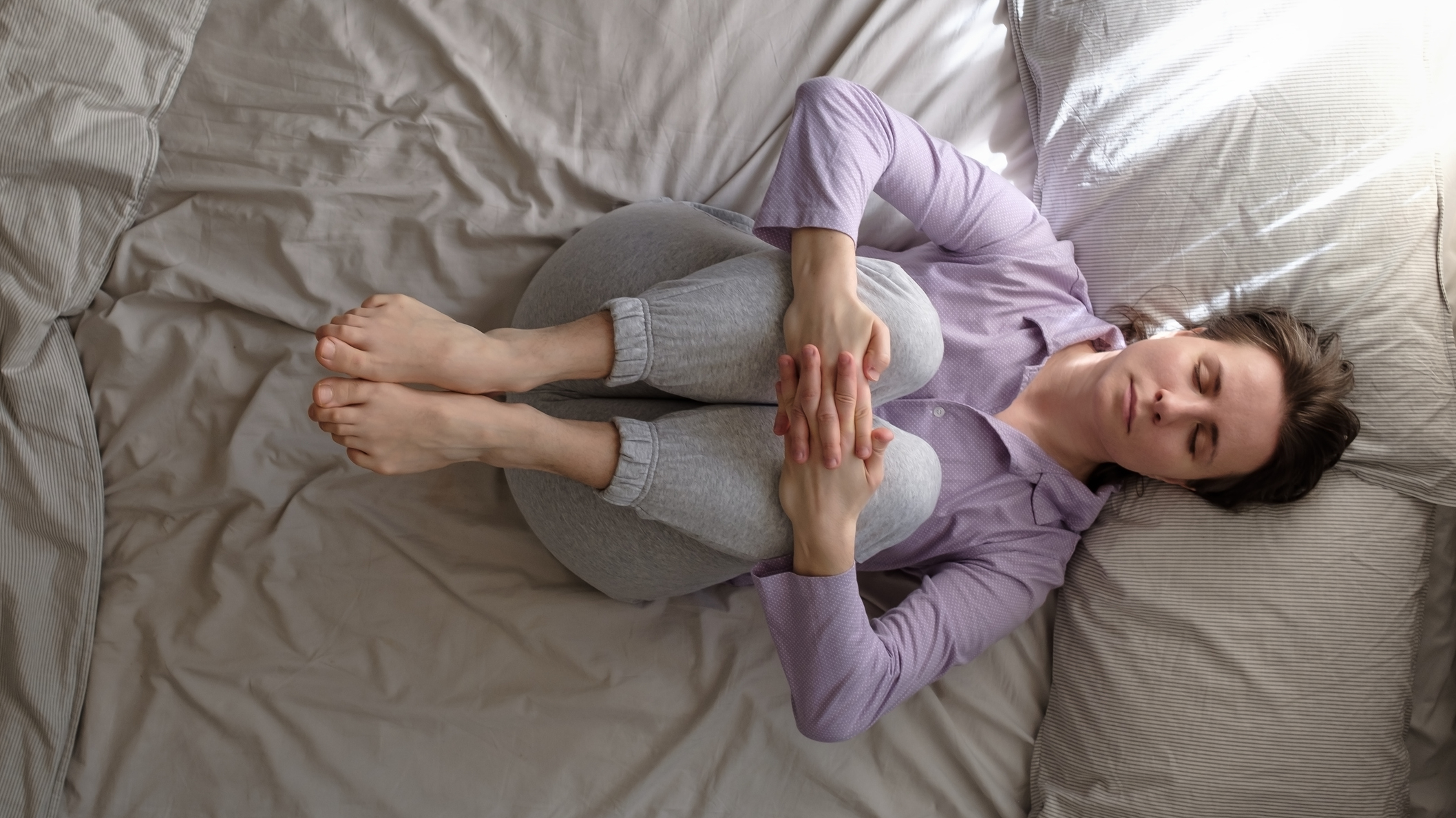 Woman in bed hugging her knees to her chest