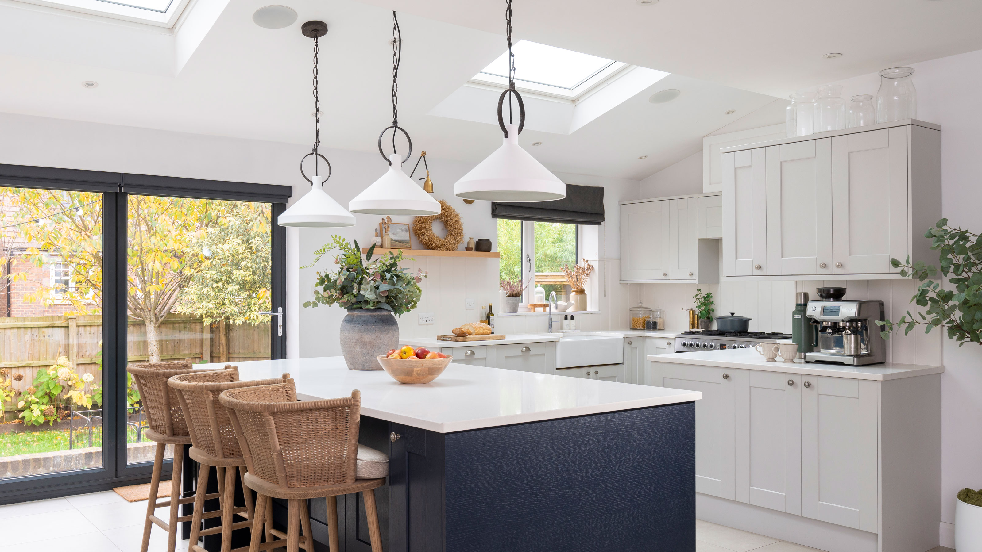 White kitchen with navy blue kitchen island white walls and three pendant lights