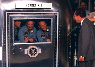Pres. Richard Nixon welcomes the Apollo 11 astronauts back to Earth after their historic voyage to the moon. The astronauts were confined within one of NASA's Mobile Quarantine Facilities for 21 days to ensure they would not contaminate Earth with any potential lunar bacteria after their short lunar sojourn.