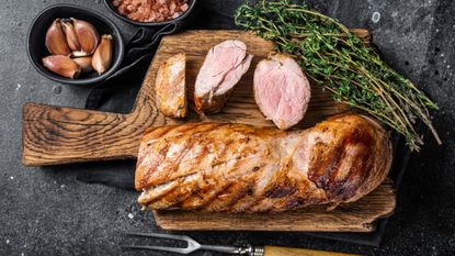 Sliced grilled pork tenderloin on a wooden cutting board with herbs, salt, and garlic 