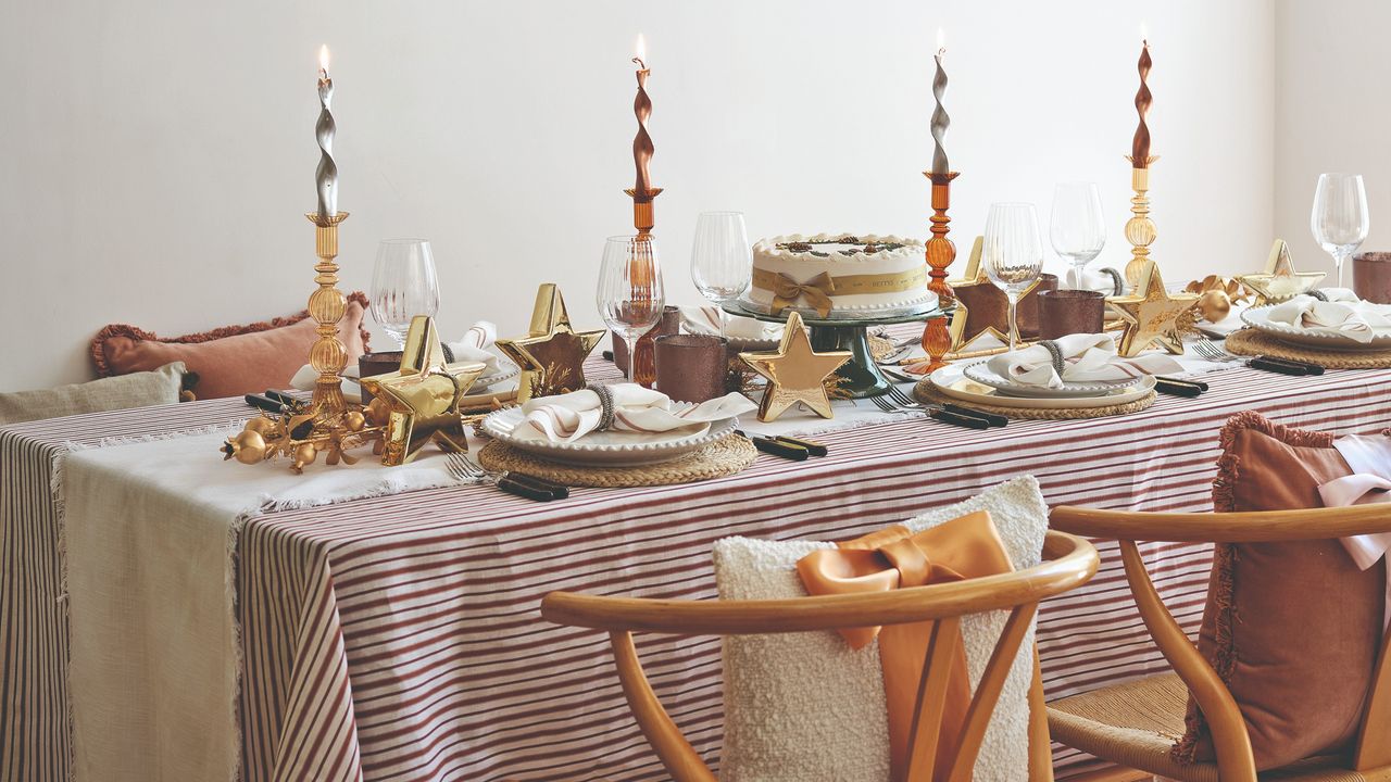 A dining table set for Christmas dinner with candlesticks, a striped tablecloth and a plain table runner with frayed edges