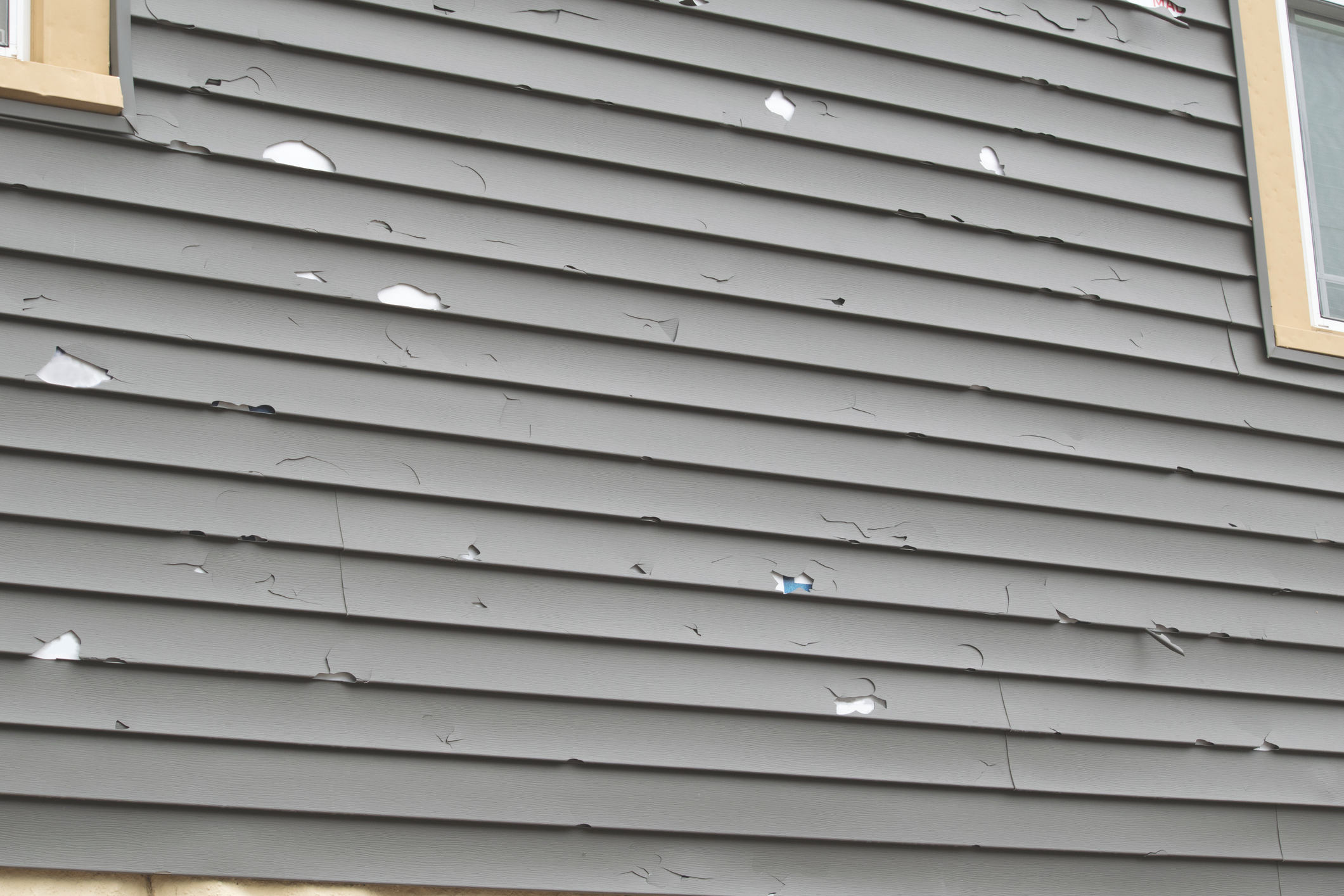 Gray siding on a house, damaged by hail.