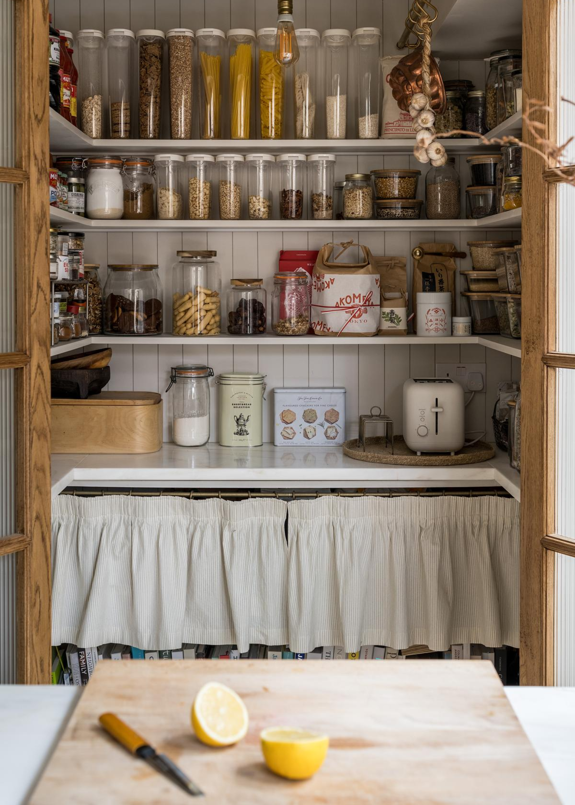 An open pantry with open shelving inside, with lots of storage jars on display with food items inside them