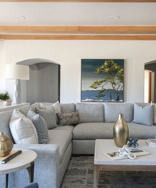 A white living room with wooden rafters, a gray sectional, and a landscape painting