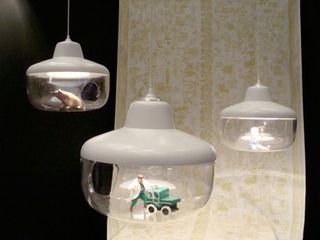 Three pendant ceiling lights with white top and glass enclosed bottoms with ornaments inside it.
