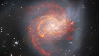 The galaxy NGC 3256 is seen as a orange, red, and yellow spiral by the James Webb Space Telescope