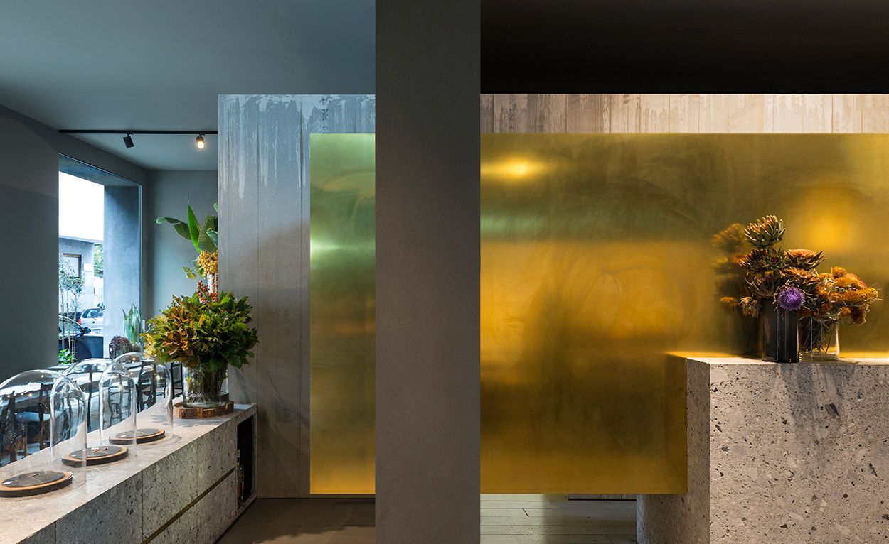 The interior of the restaurant shows the gray concrete walls with a golden backsplash and wildflowers on the countertops.