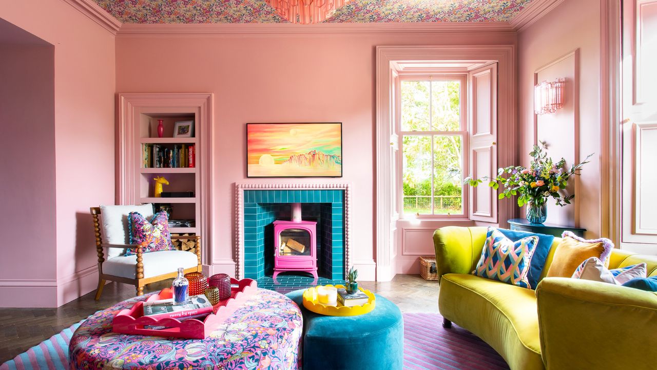 A pink-painted living room with a curved chartreuse sofa and floral ottoman complementing the floral wallpaper on the ceiling