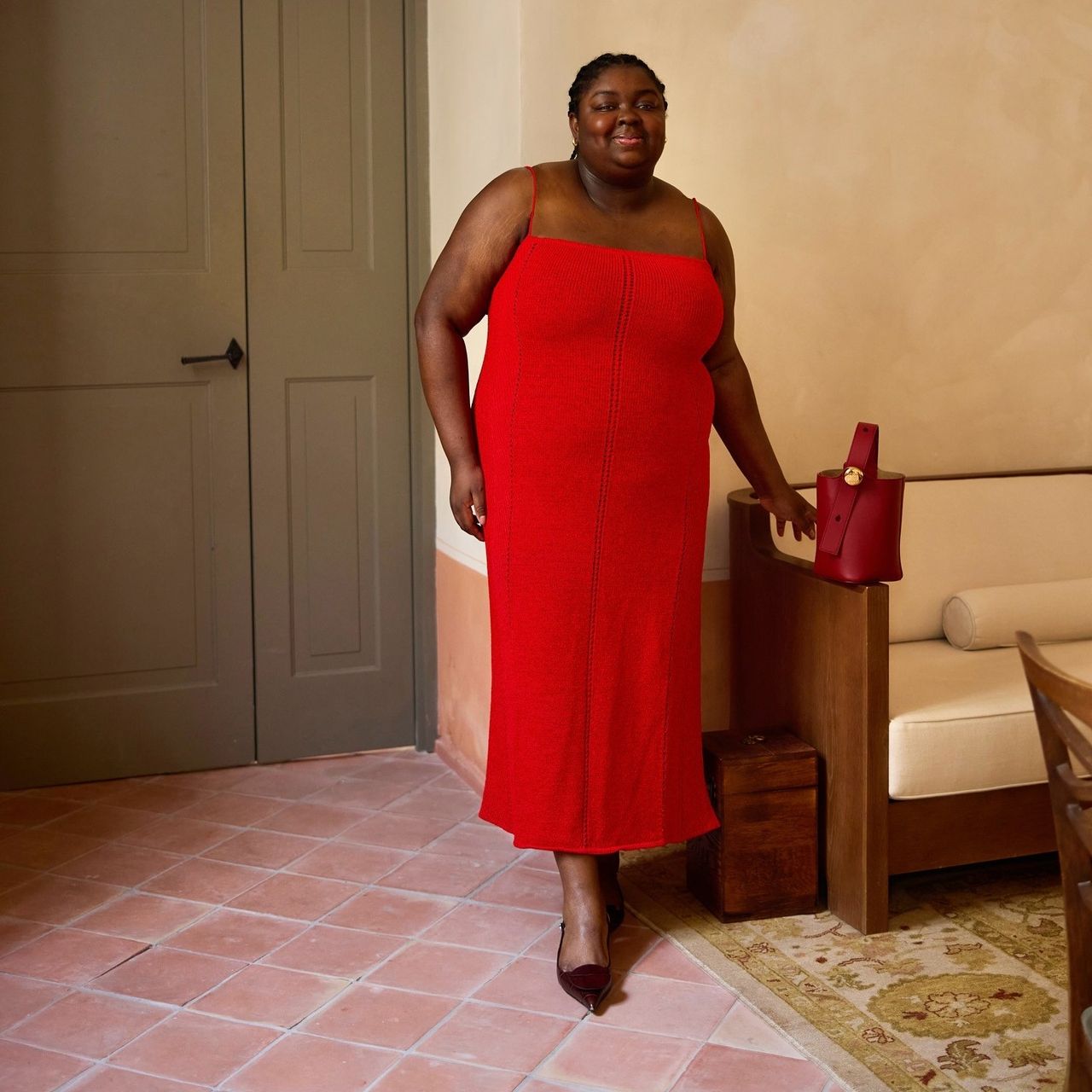 Woman wears a red pointelle column dress and black pumps. 