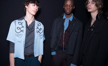 3 male models in dark clothing standing in a studio