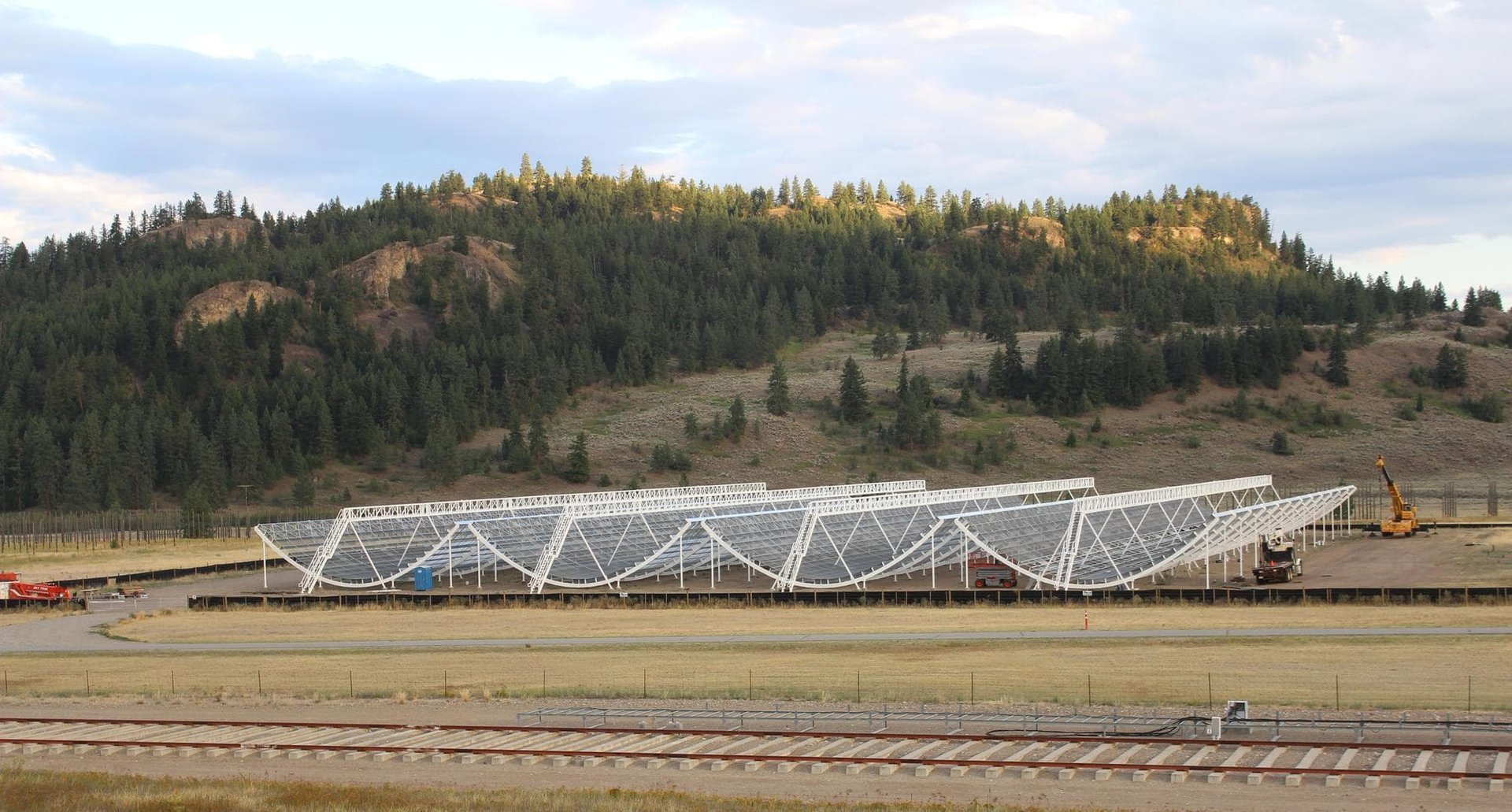 A photo of a large telescope array with a forested hill behind it
