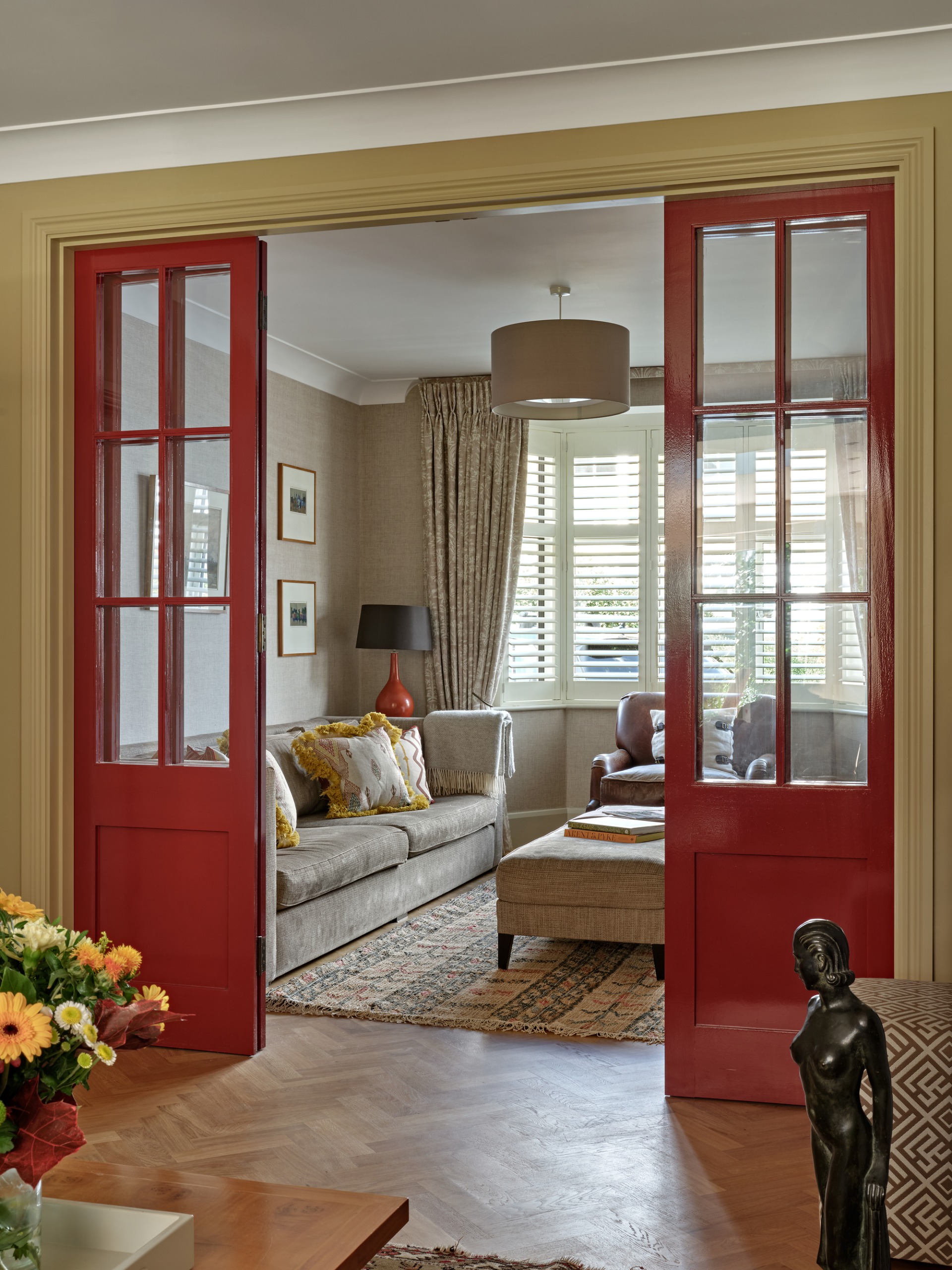 a classic-style living room with red french doors and herringbone flooring