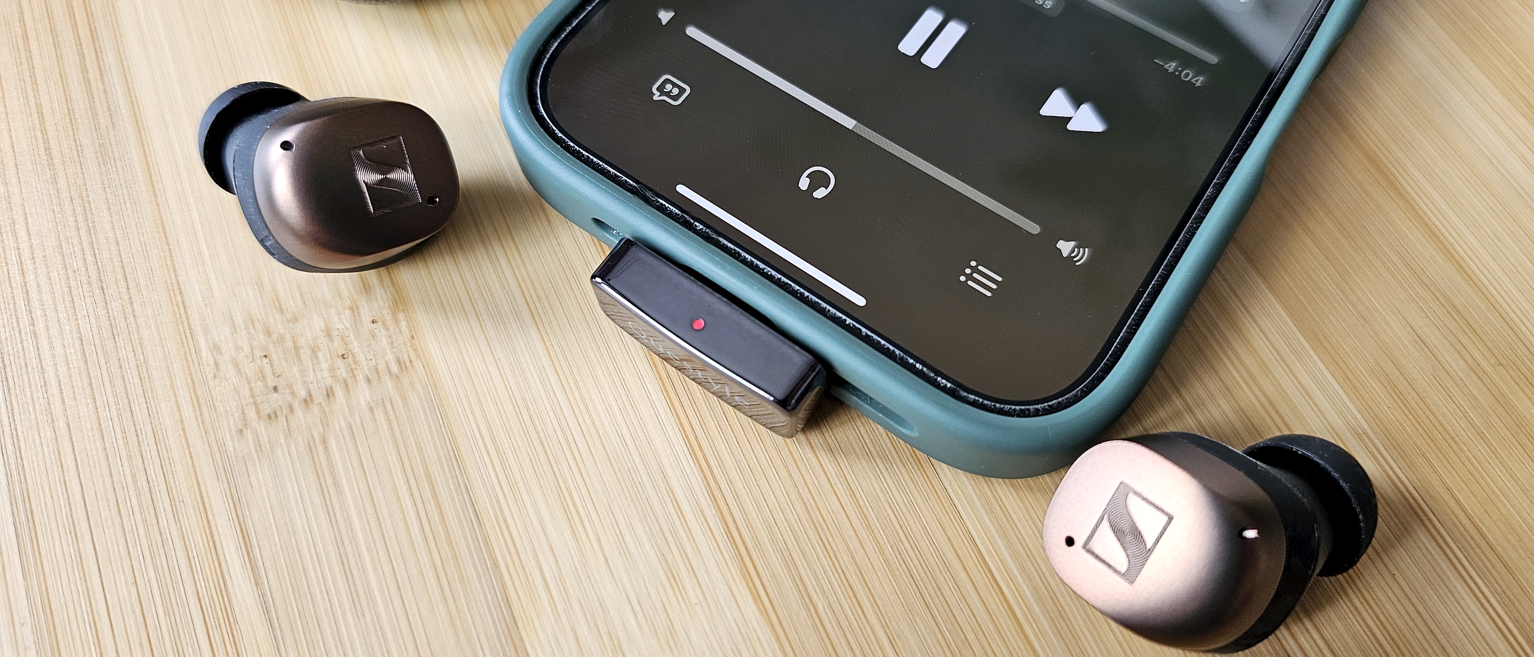 The Questyle QCC Dongle Pro with a smartphone to denote size, on a light wooden table