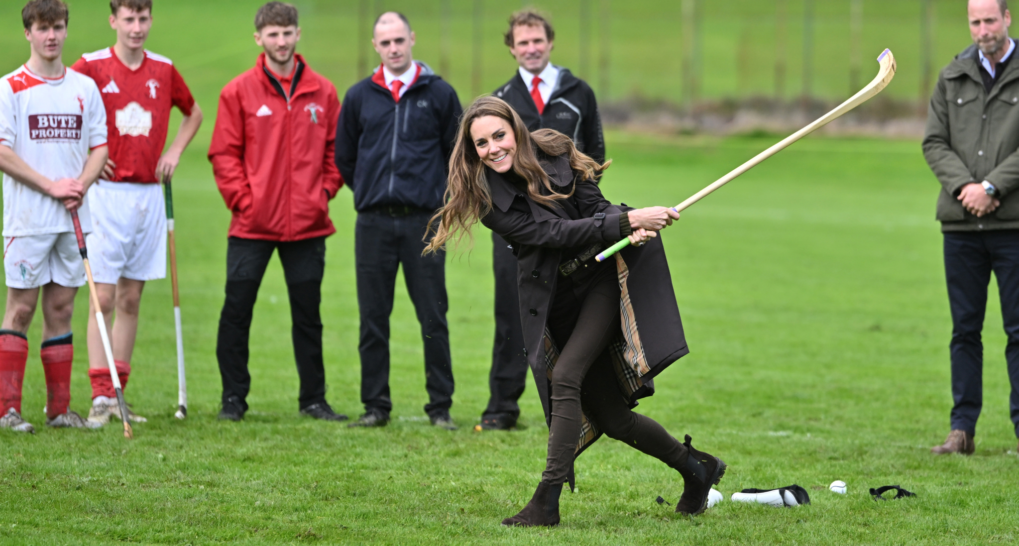 Princess Kate wearing a brown trench and skinny jeans playing hockey