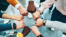 A close-up of multiple hands stacked together in a gesture of unity and collaboration. T