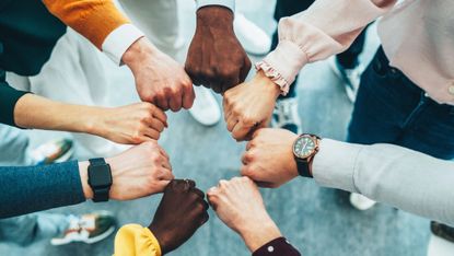 A close-up of multiple hands stacked together in a gesture of unity and collaboration. T