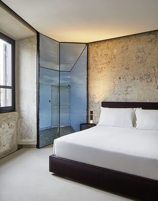 The Rooms of Rome bedroom with king bed with white bedding and untreated concrete walls