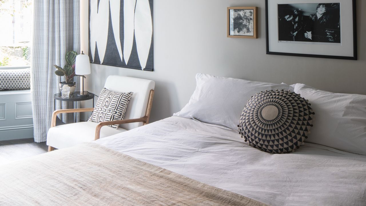 A guest bedroom with a double bed with white bed linen and a white accent chair next to the bed