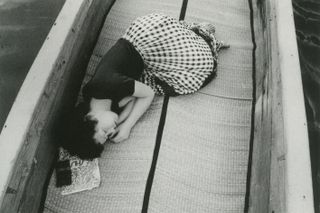 Black and white photograph of a Japanese woman sleeping in a fetal position on a boat