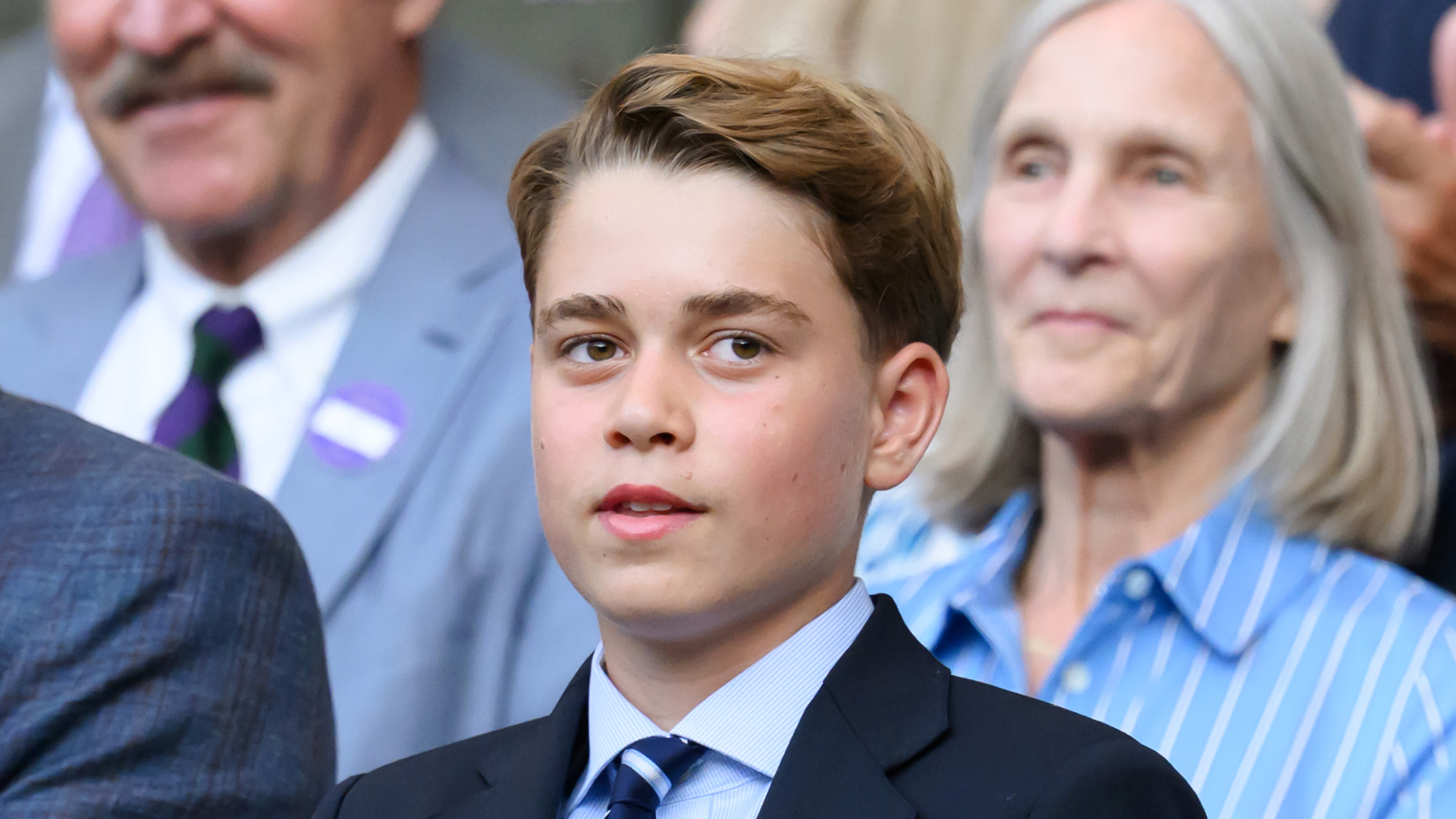 Prince George wears a navy suit with a striped tie and has floppy dark blonde hair