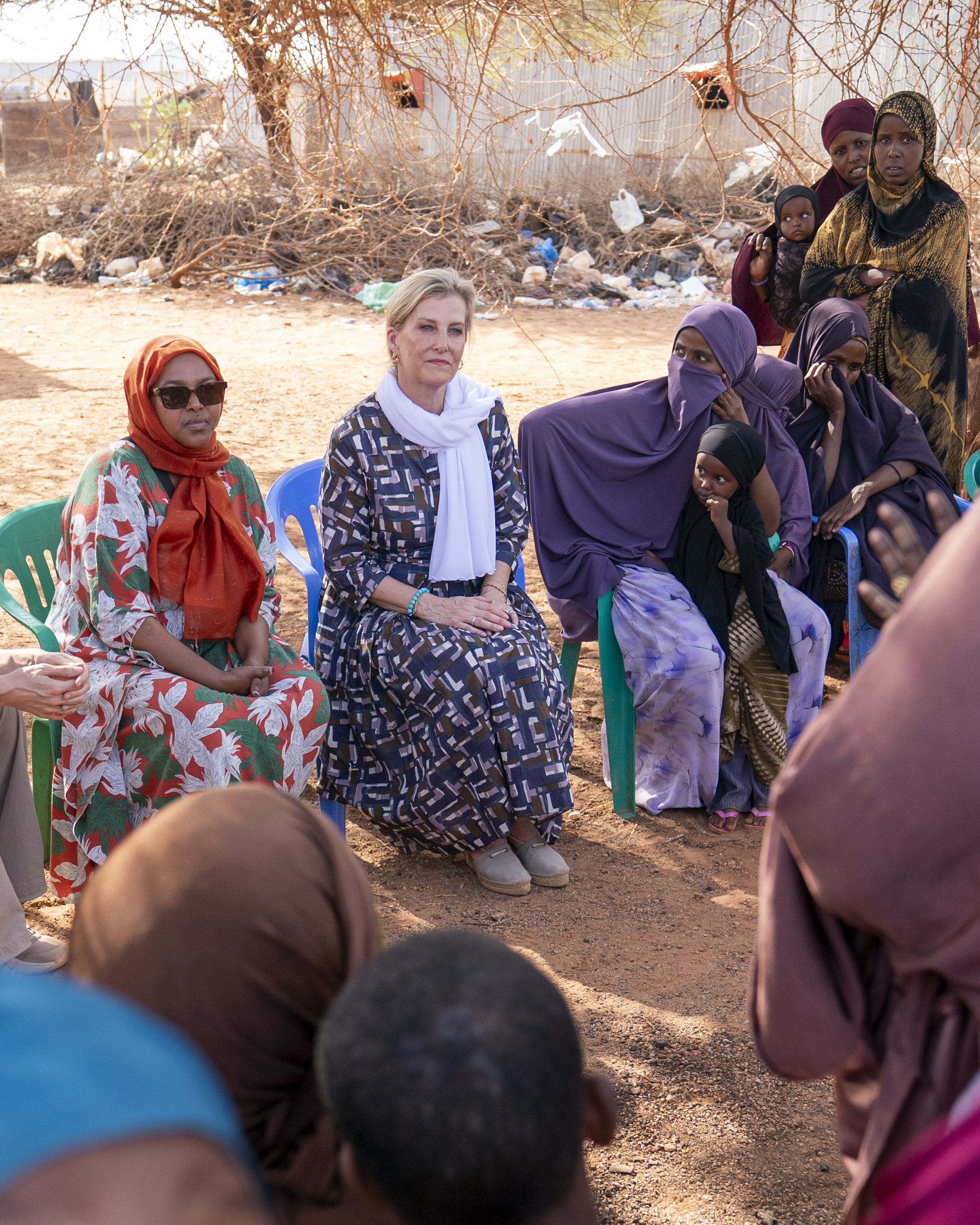 Duchess Sophie sitting in a chair wearing a blue dress and scarf with Somalian women