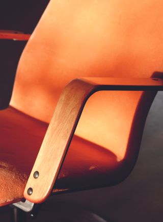 A close-up of the curved arm of a wood chair and the chair's base.