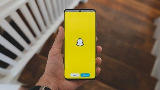 Snapchat sign-in screen on Android phone held in one hand inside a house.