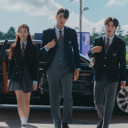 three students in private school uniforms enter a school, with a Rolls Royce sitting behind them and chauffeurs bowing, in Netflix k-drama 'Hierarchy'
