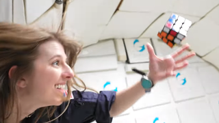 woman reaches out for rubik's cube during microgravity flight