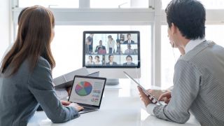 To personer deltager i en videokonference med andre personer på skærmen.